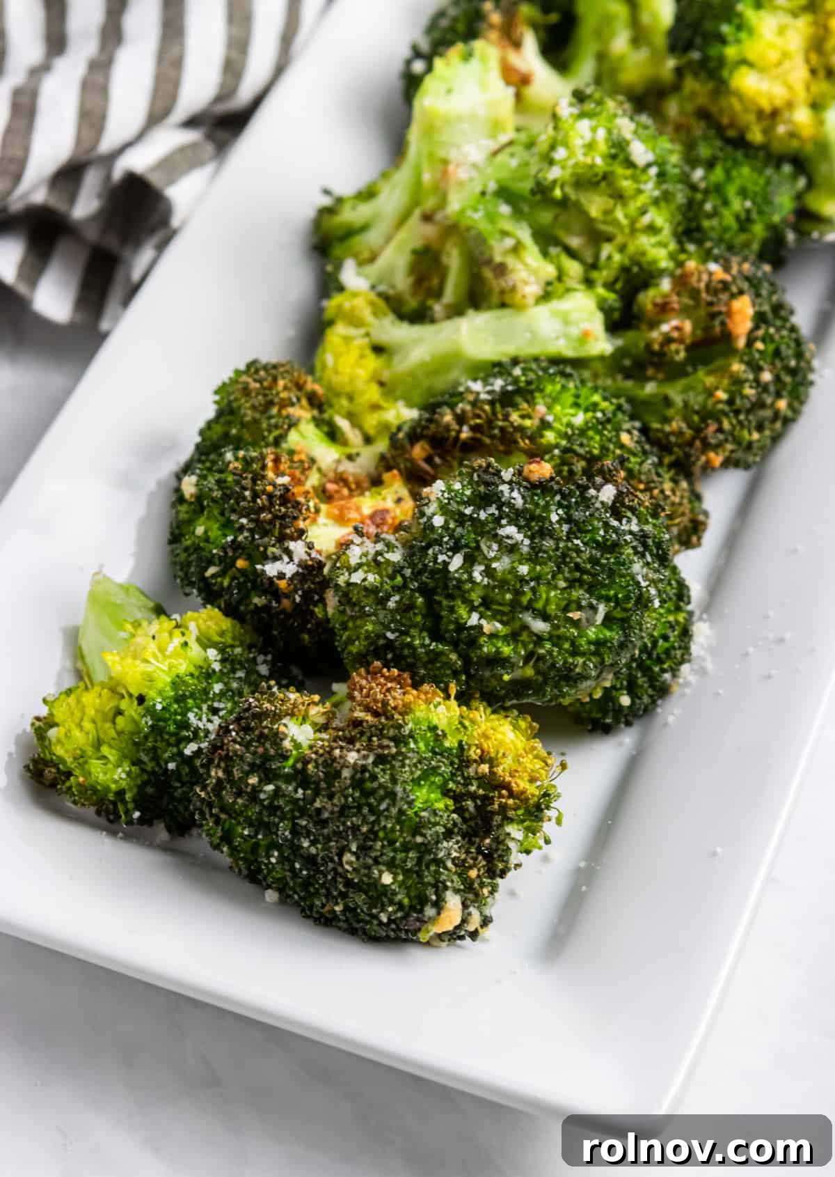 Easy Crispy Air Fryer Broccoli 6 A close-up shot of a plate filled with crispy Air Fryer Parmesan Broccoli, garnished with extra grated Parmesan cheese.