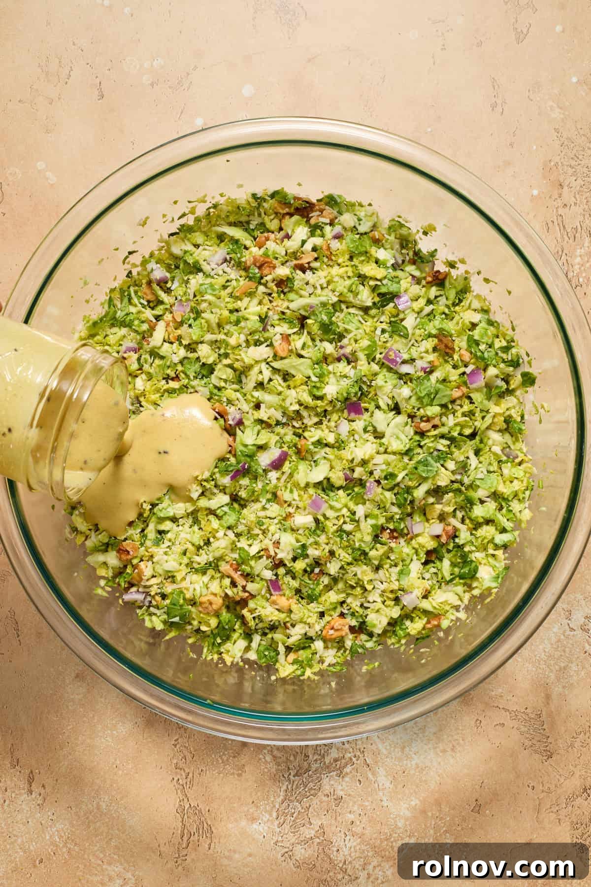 Zesty Brussels Sprout Slaw 9 Dressing being poured over shredded brussels sprouts salad before tossing.