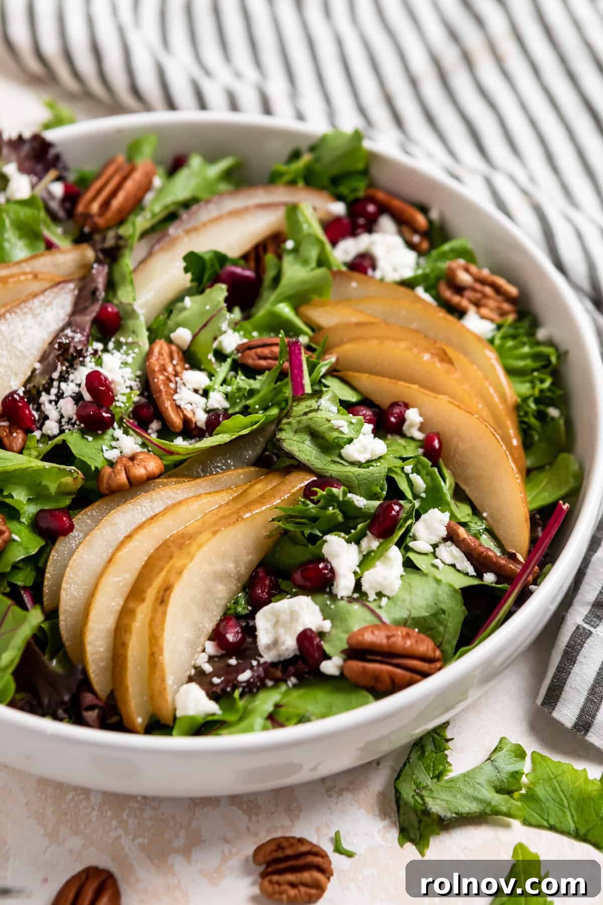 Golden Roasted Pear Salad 2 White salad bowl with spring greens, roasted pears, pomegranates, goat cheese and pecans.