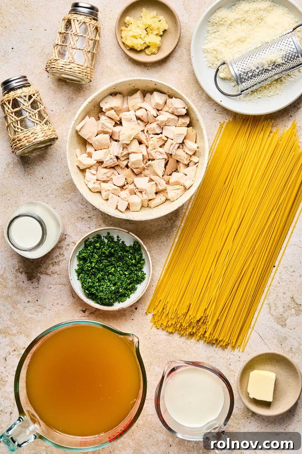 Effortless Creamy Chicken Alfredo 3 Pasta, chicken cubed, broth, parsley and other ingredients arranged on surface.