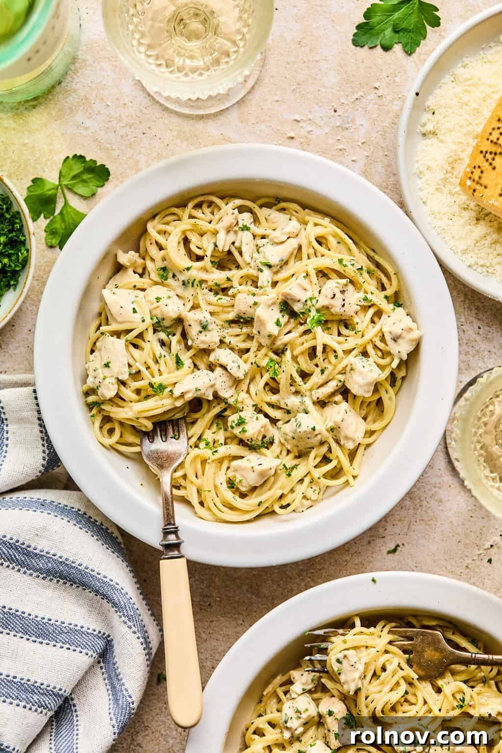 Effortless Creamy Chicken Alfredo 6 Bowl of chicken Alfredo with napkin, wine, parsley and other ingredients surrounding it.