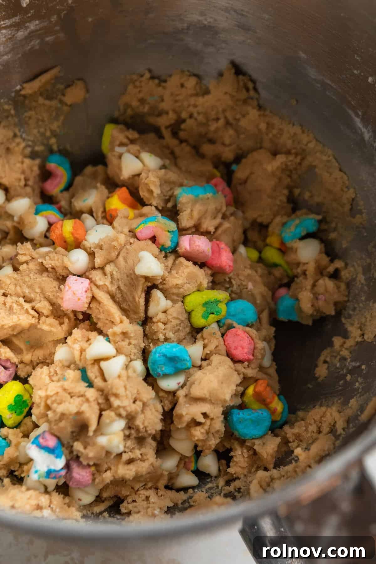 Charmed Bites 3 Creamy Lucky Charm cookie dough, studded with colorful marshmallows, patiently waits in a mixing bowl, ready for its transformation into delicious cookies.