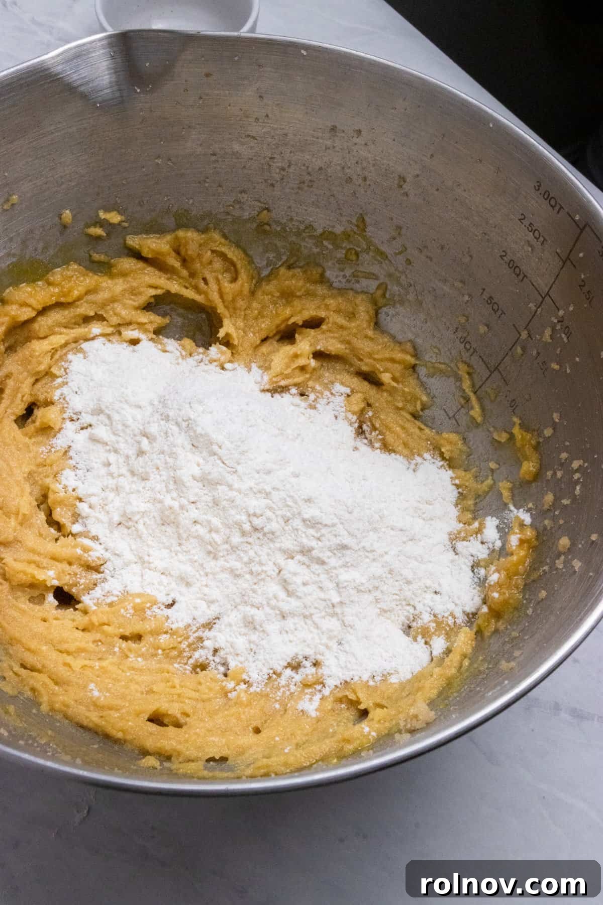 Charmed Bites 7 Dry ingredients, including flour, baking soda, and salt, freshly added to the wet mixture in the mixing bowl, ready to be combined into a cohesive cookie dough.