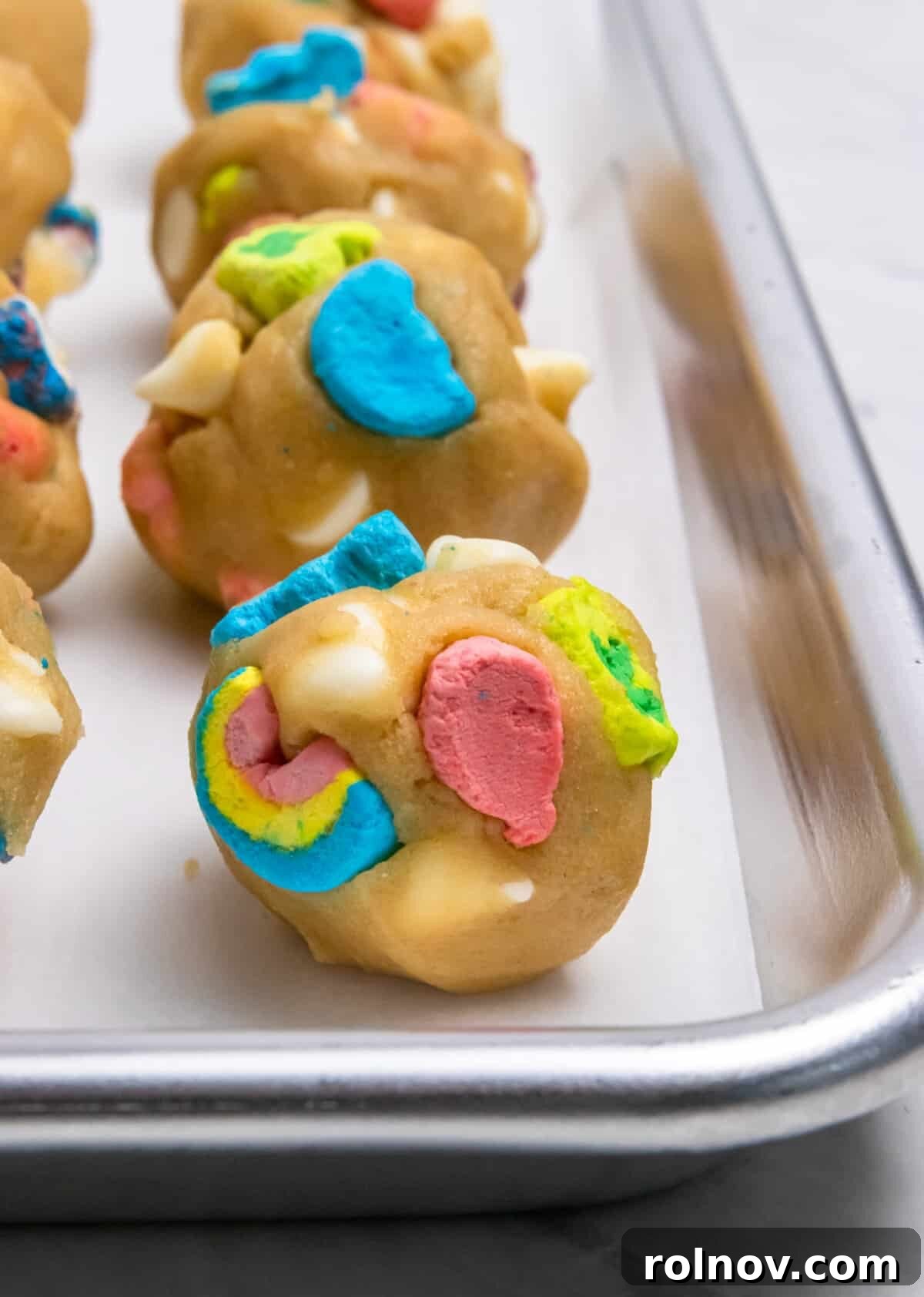 Charmed Bites 10 Perfectly scooped balls of Lucky Charm cookie dough, arranged neatly on a parchment-lined baking sheet, awaiting their turn in the oven.