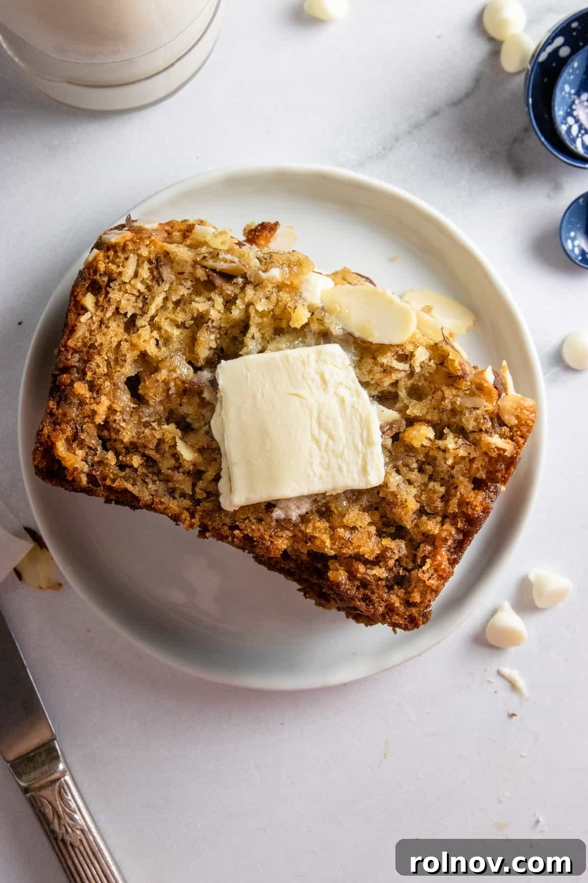 A perfectly baked slice of banana bread, made with ripe bananas, artfully arranged on a plate with a dollop of butter, ready to be enjoyed.