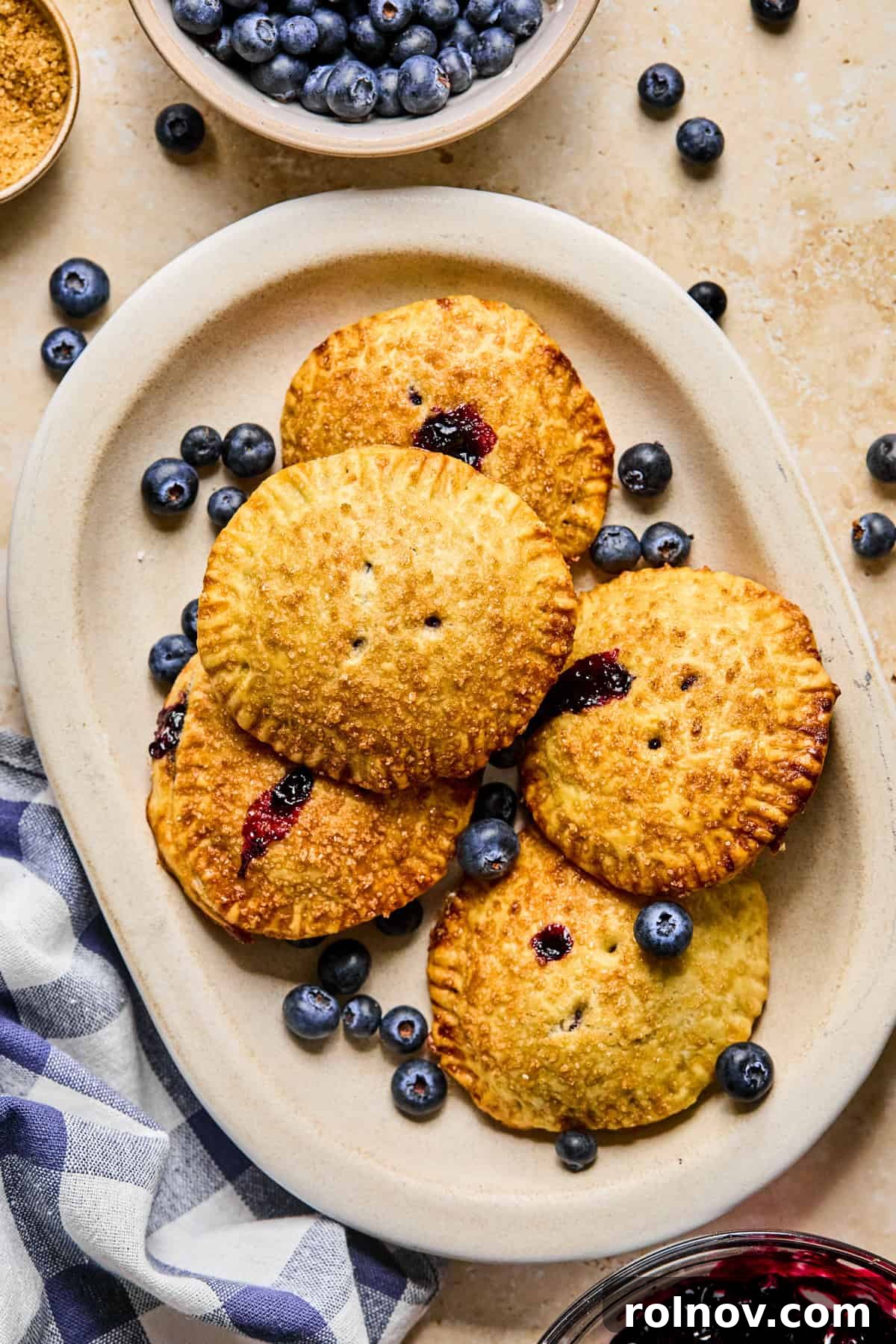 Crispy Air-Fried Blueberry Turnovers 17 A plate of freshly baked blueberry hand pies, with a bowl of fresh blueberries next to it, invitingly presented.