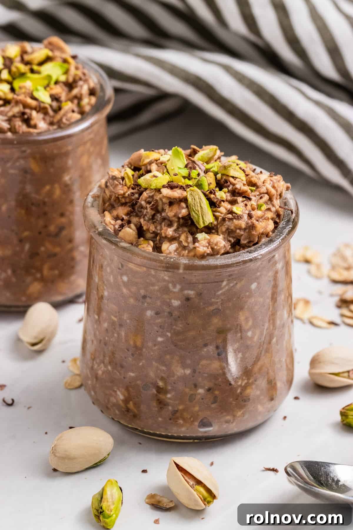 Decadent Chocolate Pistachio Overnight Oats 2 A charming jar filled with Chocolate Pistachio Overnight Oats, topped with vibrant green pistachios and surrounded by their cracked shells, ready for a delicious breakfast.