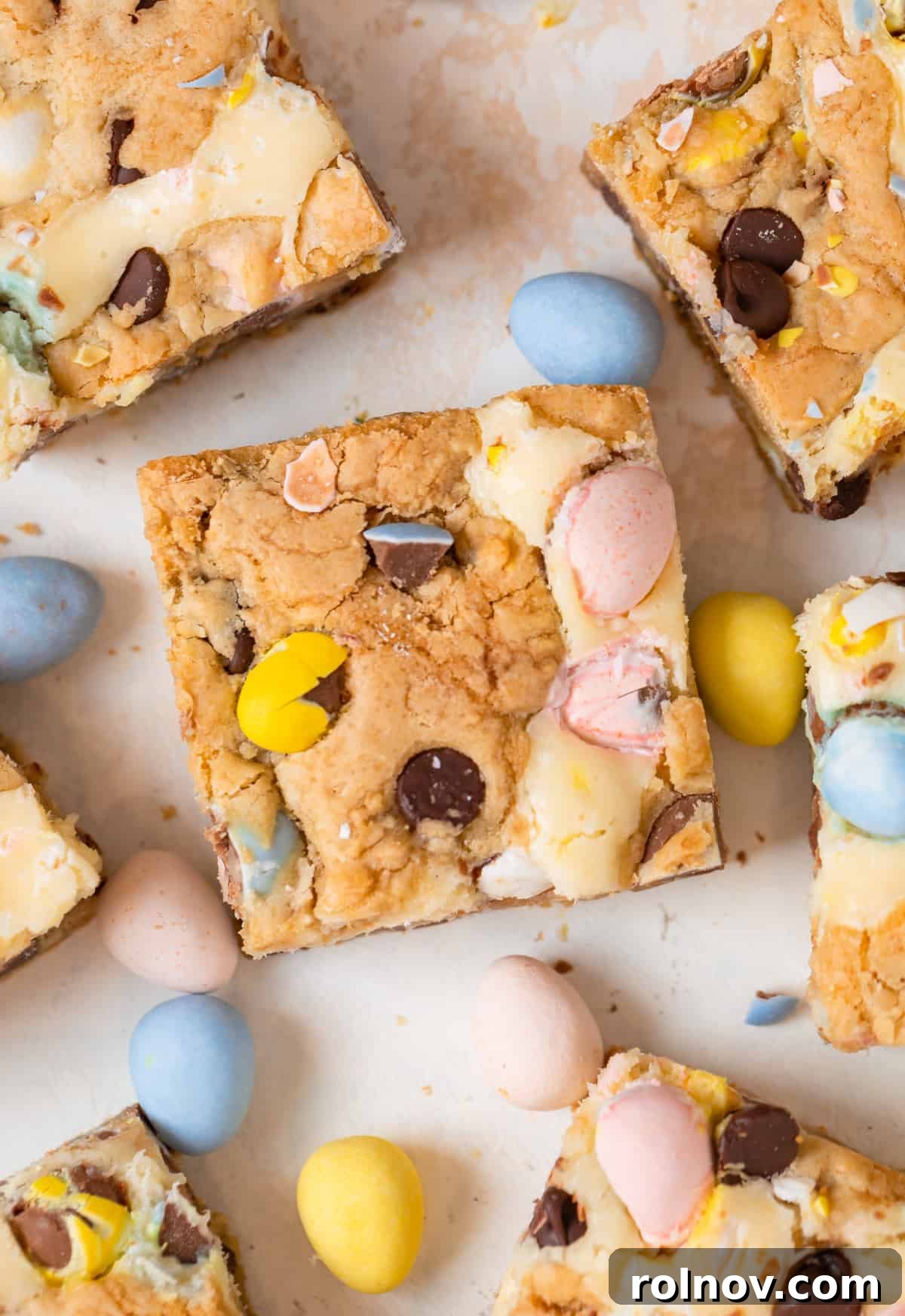 Easter Mini Egg Cheesecake Bars 2 Mini egg bars with chocolate chips and cheesecake swirl cut with mini eggs surrounding.