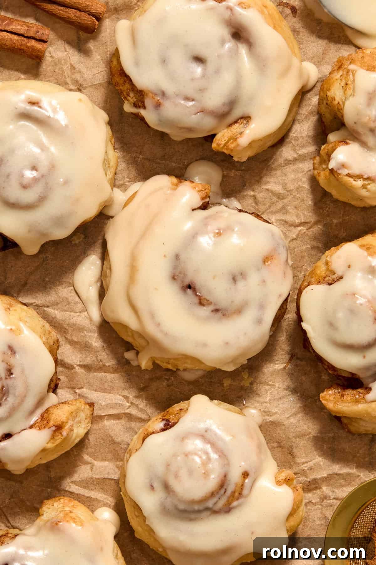 Flaky Cinnamon Swirls 2 Cinnamon rolls with icing on top on parchment.