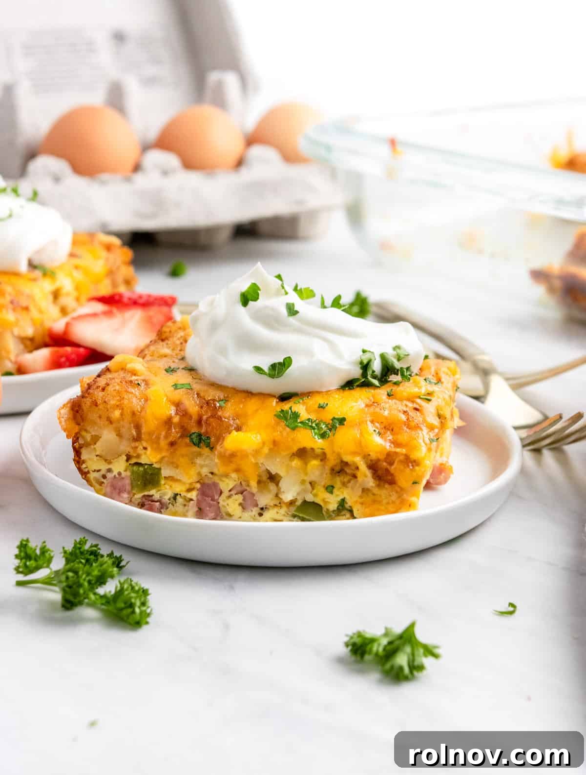 Crispy Tater Tot Breakfast Bake 2 Delicious Ham and Cheese Breakfast Casserole with Crispy Tater Tots, served with a dollop of sour cream on a white plate, ready for breakfast or brunch.
