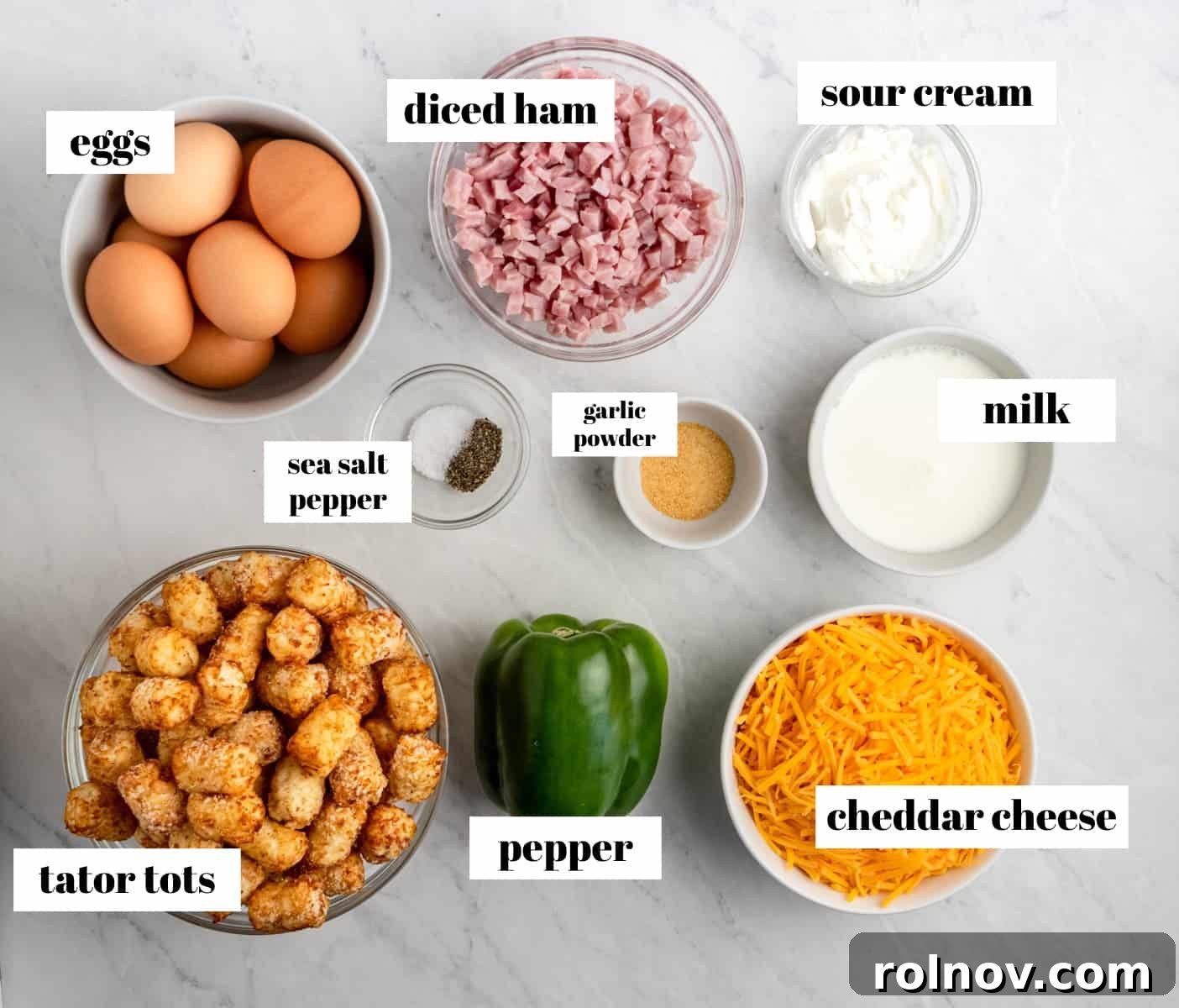 Crispy Tater Tot Breakfast Bake 3 Individual ingredients for Ham and Cheese Breakfast Casserole with Tater Tots, including eggs, ham, bell pepper, milk, and cheese, neatly arranged on a kitchen counter.