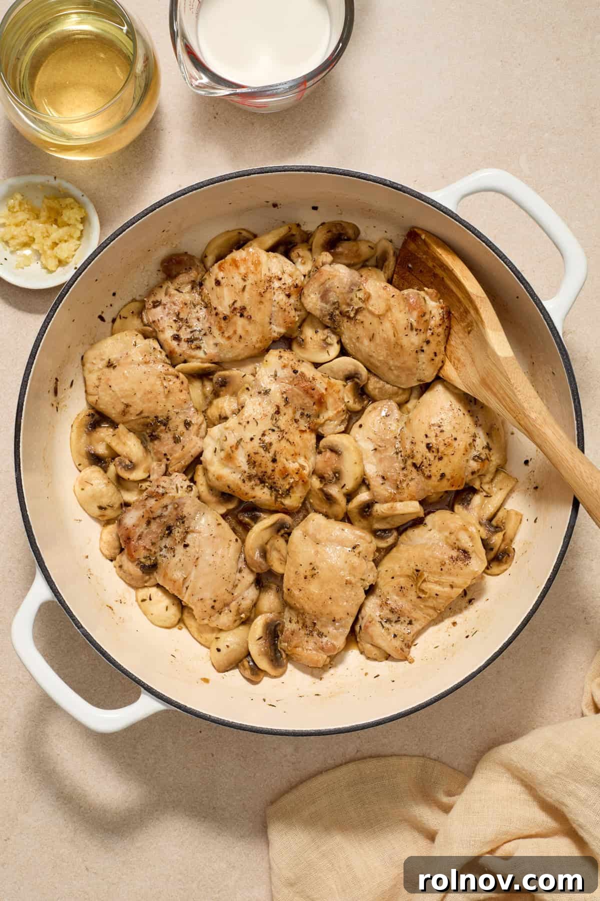Golden Chicken Thighs in Velvety Mushroom Sauce 6 Mushrooms added to skillet with chicken thighs and wooden spoon propped in the pan.
