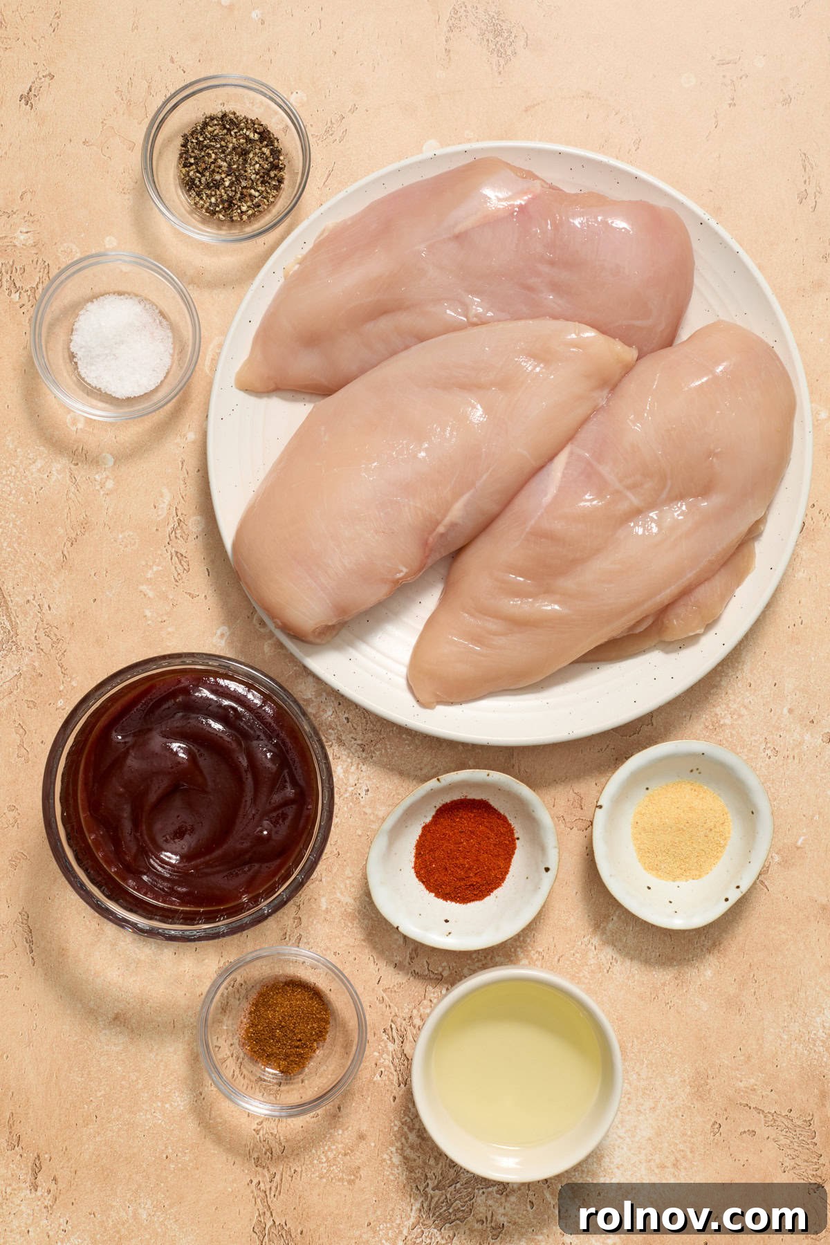 Raw chicken breasts, bbq sauce, seasoning and oil on surface.