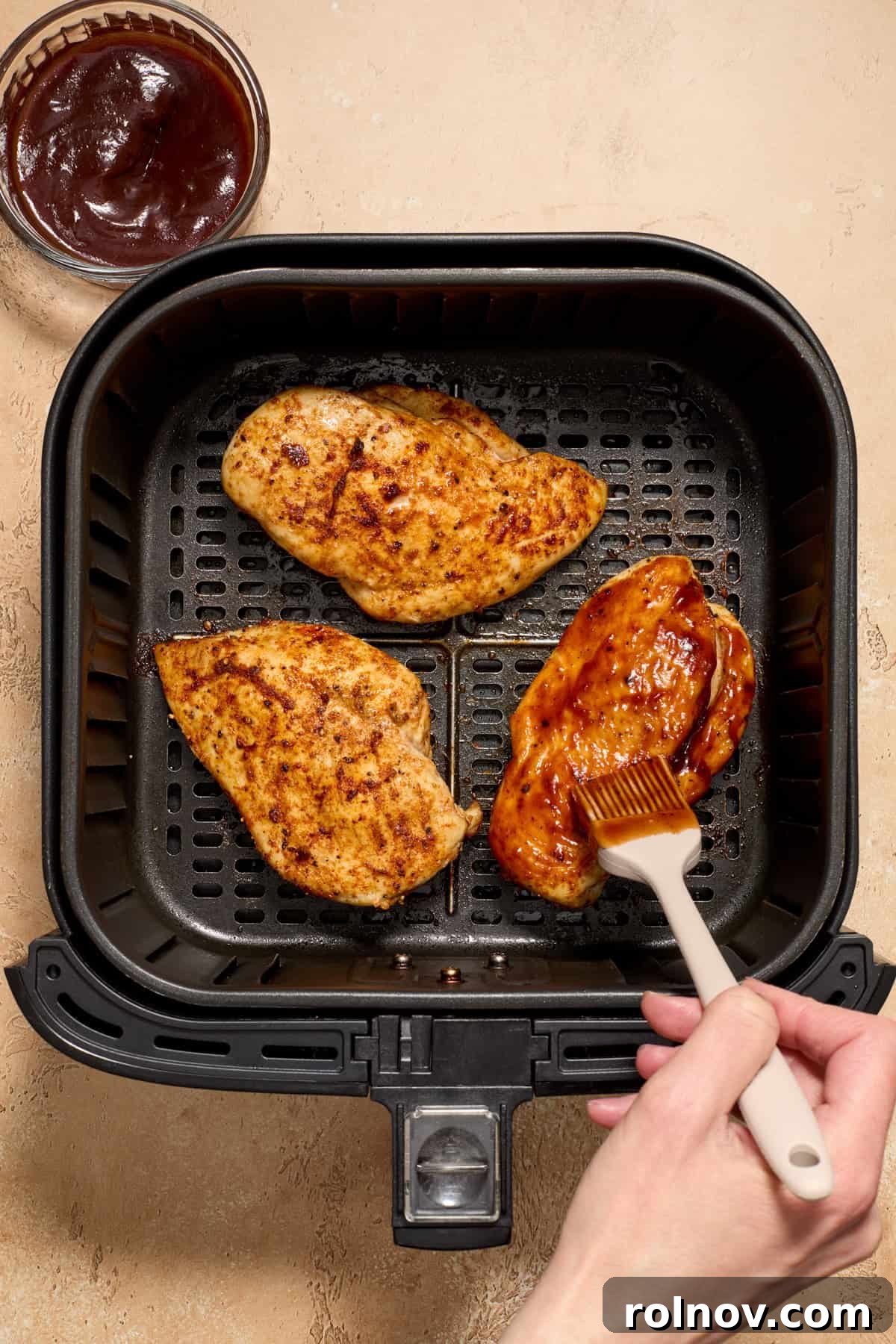 Air fryer basket with chicken with bbq sauce being brushed over top.