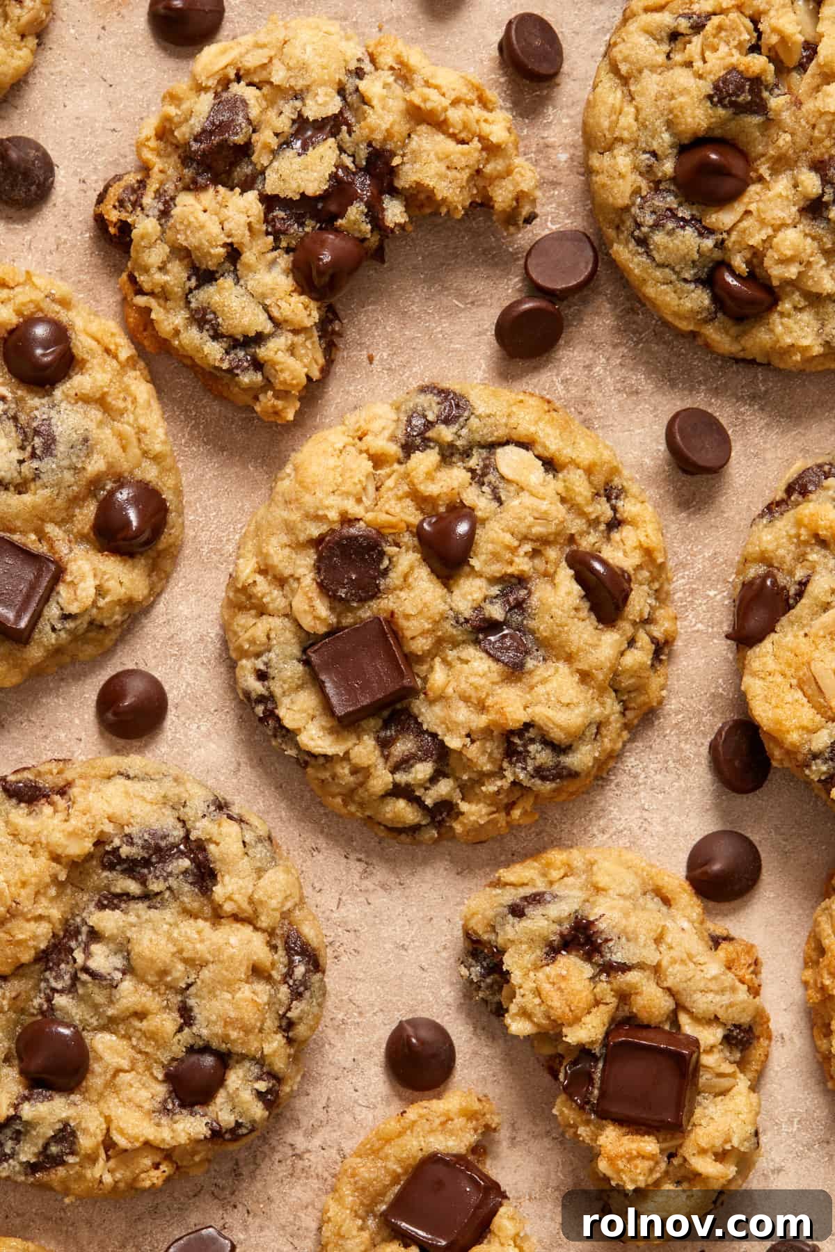 Almond & Oat Harmony Gluten-Free Chip Cookies 11 Oatmeal chocolate chip cookies generously arranged on a surface, with extra chocolate chips scattered around for a decadent display.