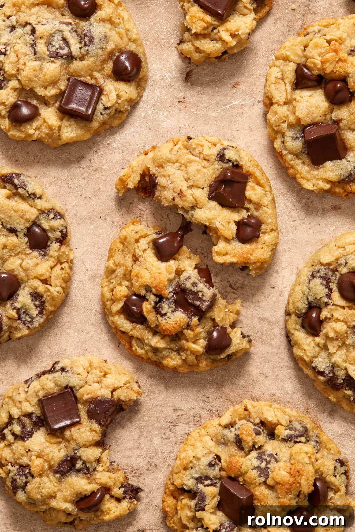 Almond & Oat Harmony Gluten-Free Chip Cookies 3 Cookies arranged on a surface with a focus on a center cookie that is broken into two pieces, revealing gooey, melty chocolate chips within.