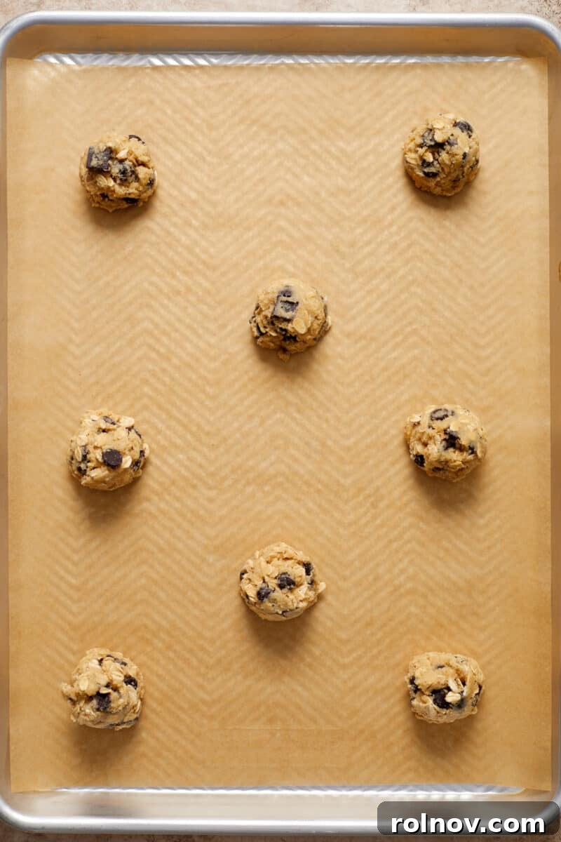 Almond & Oat Harmony Gluten-Free Chip Cookies 9 Oatmeal chip cookie dough rolled into neat balls and arranged on a parchment-lined cookie sheet, ready for baking.