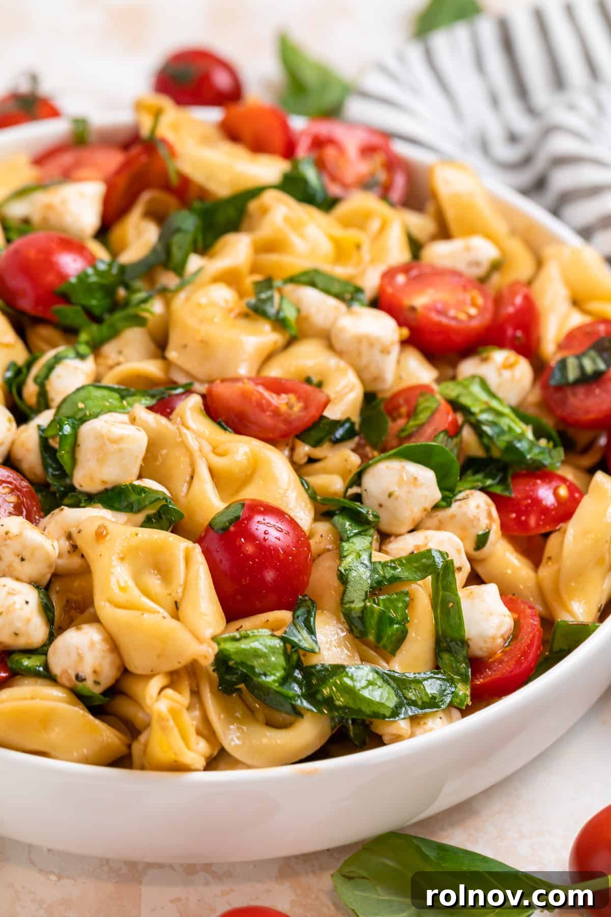 Fresh Tortellini Caprese Salad in a white bowl, garnished with halved cherry tomatoes, fresh mozzarella pearls, and basil leaves, ready to be served.