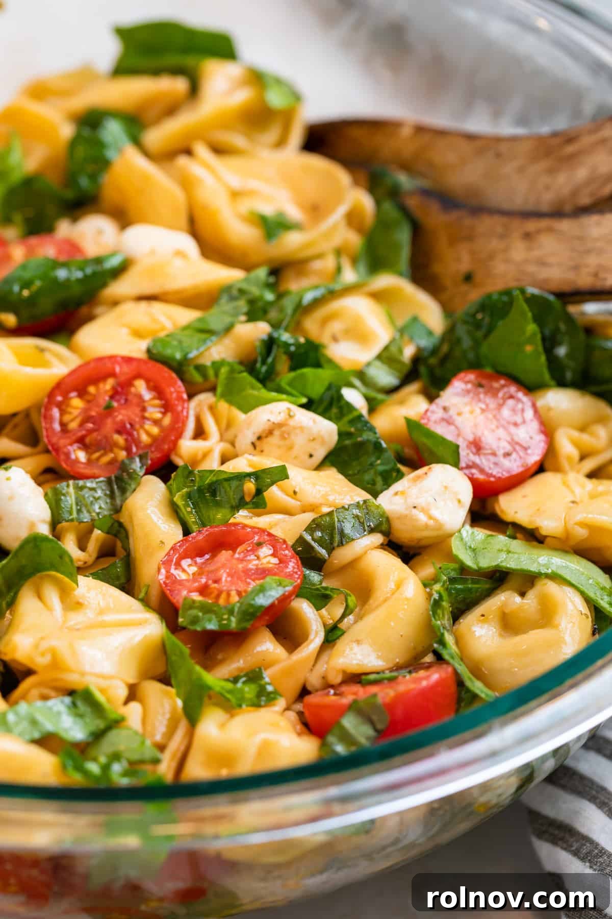Tortellini caprese salad in glass bowl with wood spoons.