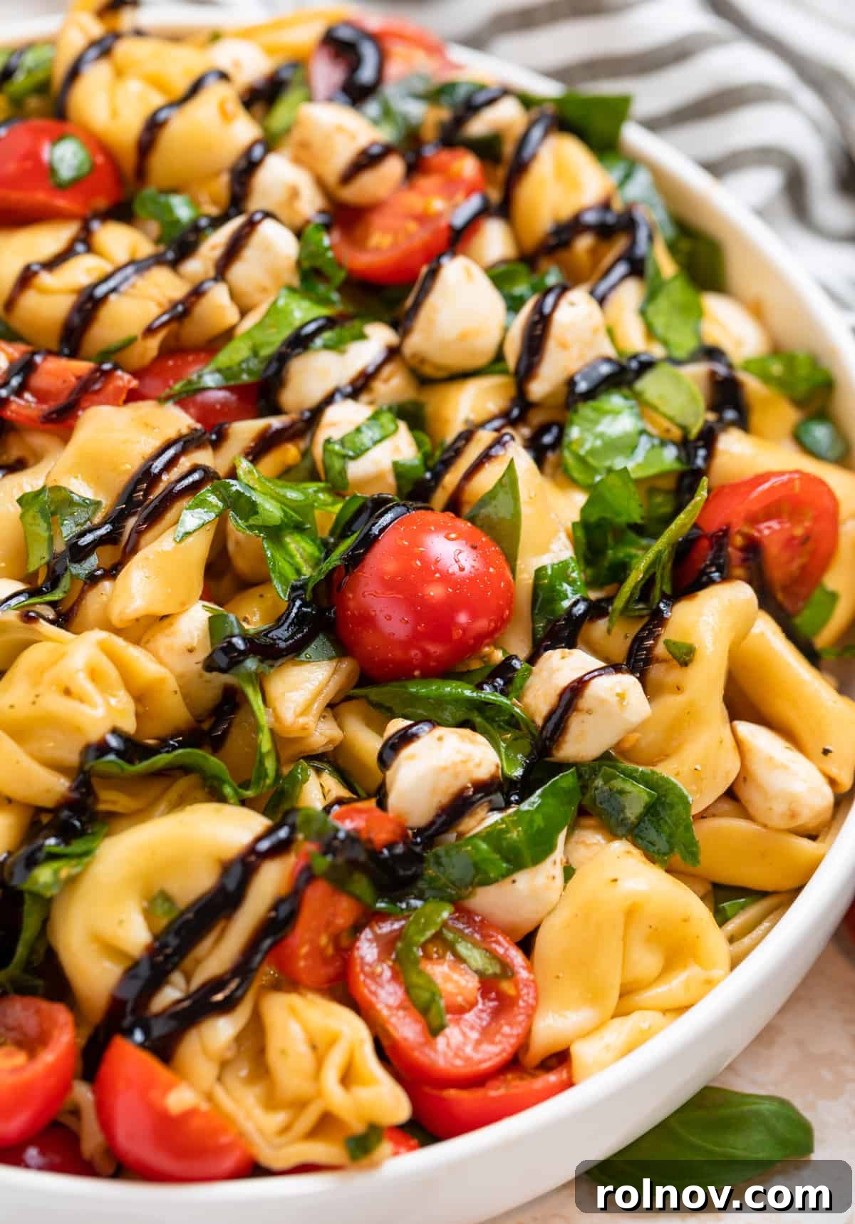 Tortellini pasta salad in white bowl with balsamic glaze drizzled on top.