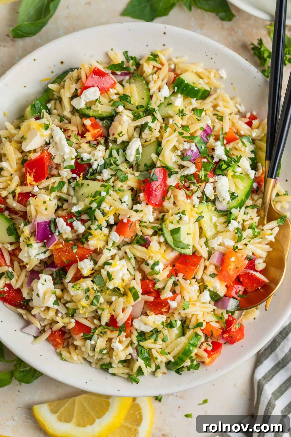 Bright & Effortless Lemon Orzo Salad with Feta 2 Overhead view of lemon orzo salad with fresh parsley and feta, garnished with lemon slices.