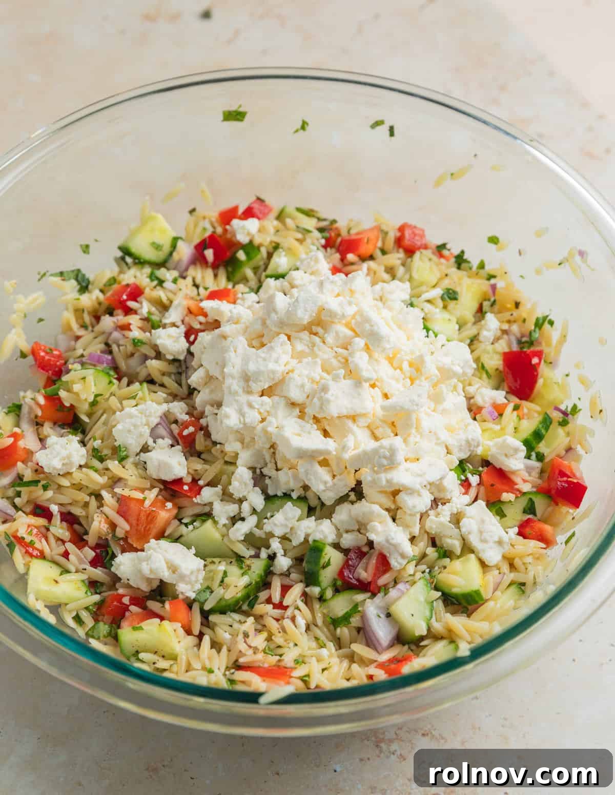 Bright & Effortless Lemon Orzo Salad with Feta 7 Feta added over top of salad mixture in bowl, ready to be folded in.