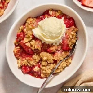 Strawberry crumble served in bowl with a scoop of ice cream and spoon scooping in.