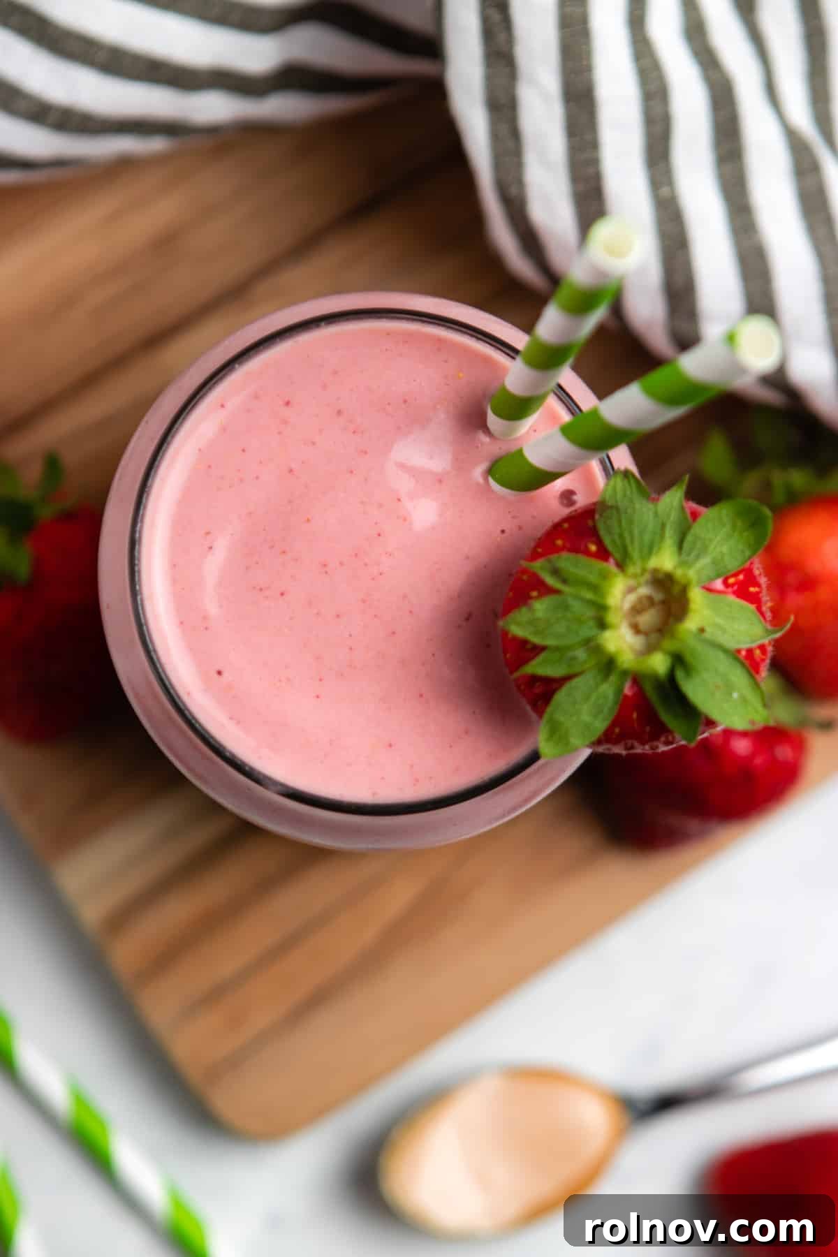 Strawberry Nut Bliss Smoothie 2 Overhead view of strawberry peanut butter smoothie on wood board with straw.