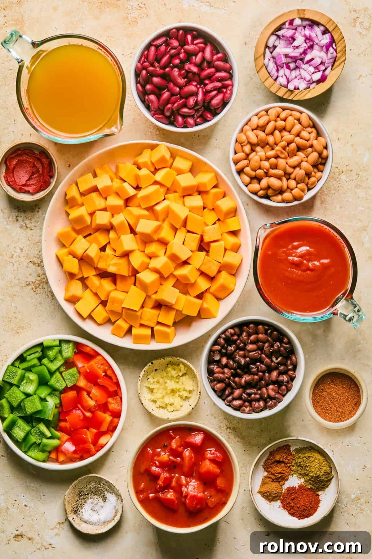 A vibrant selection of chili ingredients laid out on a surface, including beans, rich broth, pre-cubed butternut squash, colorful bell peppers, and various aromatic seasonings.
