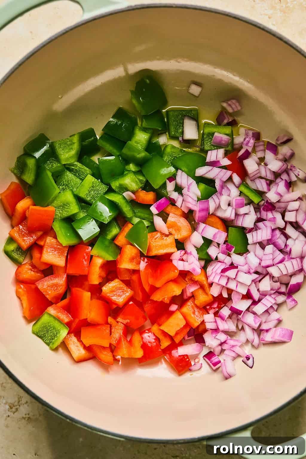 Red onion and bell peppers being sautéed in a large Dutch oven pot on the stovetop.