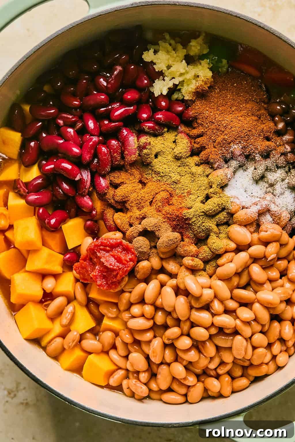 All the remaining ingredients, including beans, butternut squash cubes, canned tomatoes, and seasonings, have been added to the stockpot with the sautéed vegetables.