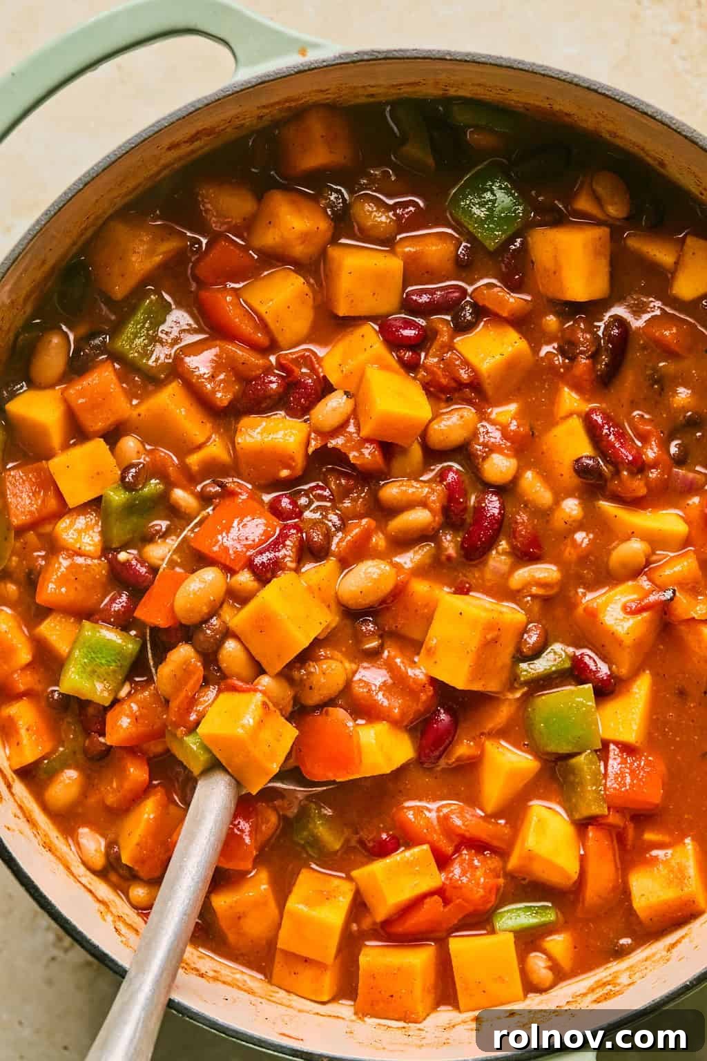 A large spoon scooping into a rich, cooked butternut squash chili simmering in a pot.
