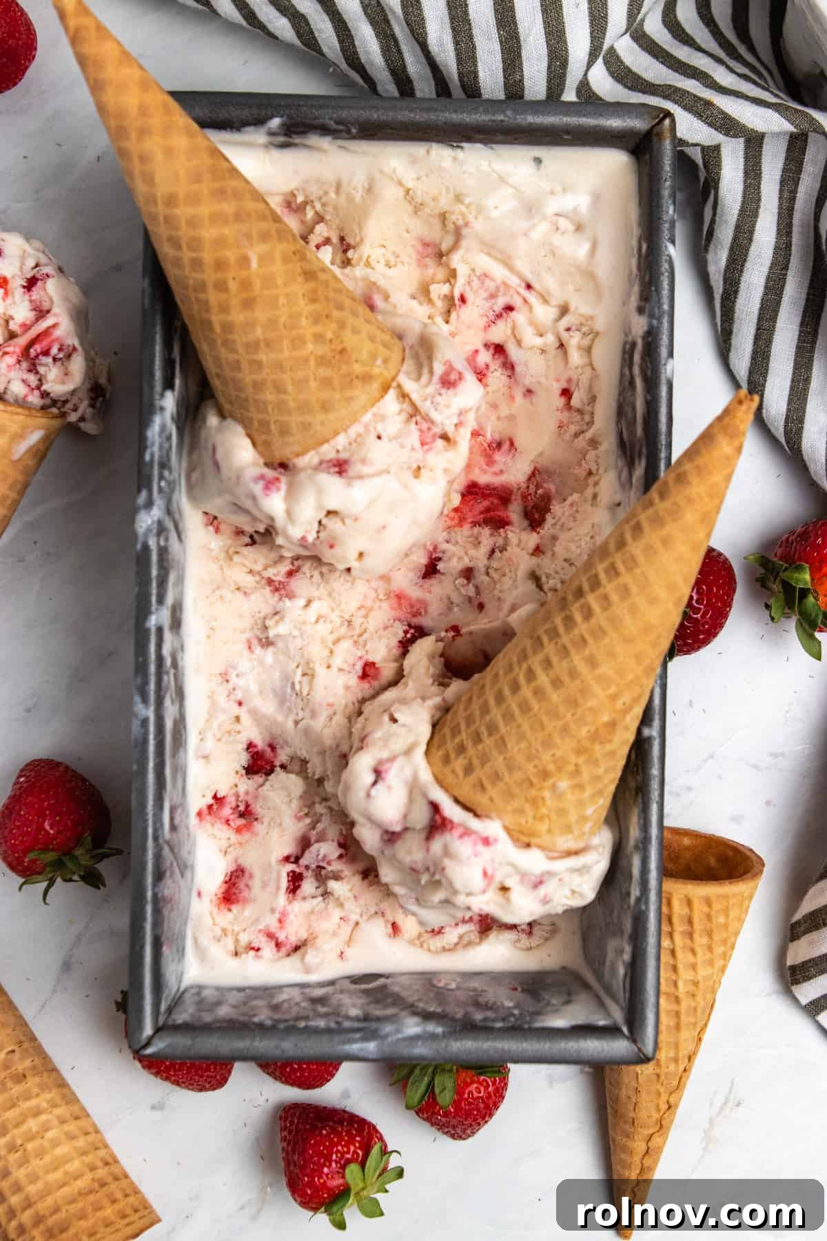 Easy Homemade No-Churn Strawberry Delight 2 Strawberry ice cream served in a bread loaf pan with multiple scoops, accompanied by sugar cones, highlighting its readiness to be enjoyed.