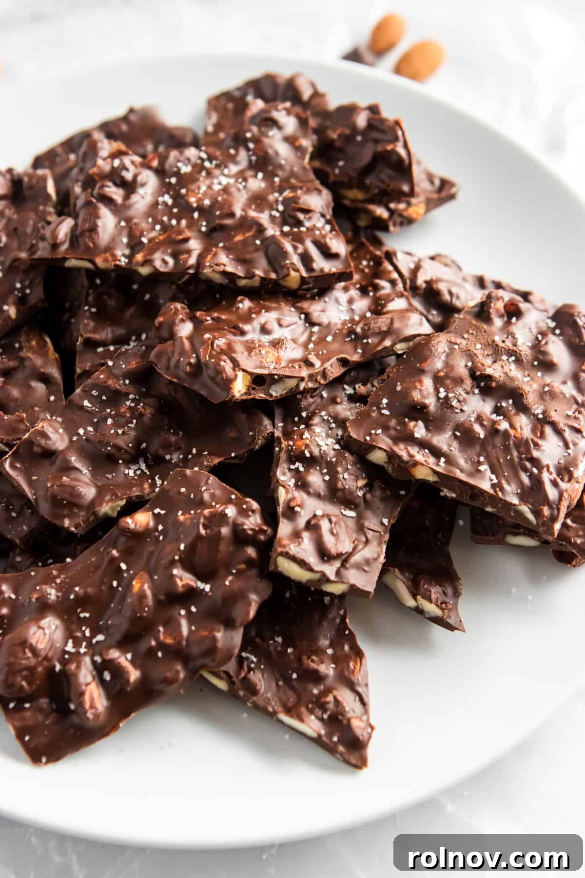 Sweet and Salty Dark Chocolate Almond Bark Thins 3 Close-up of copycat Bark Thins on a pristine white plate, showcasing their inviting texture and sea salt sprinkles.