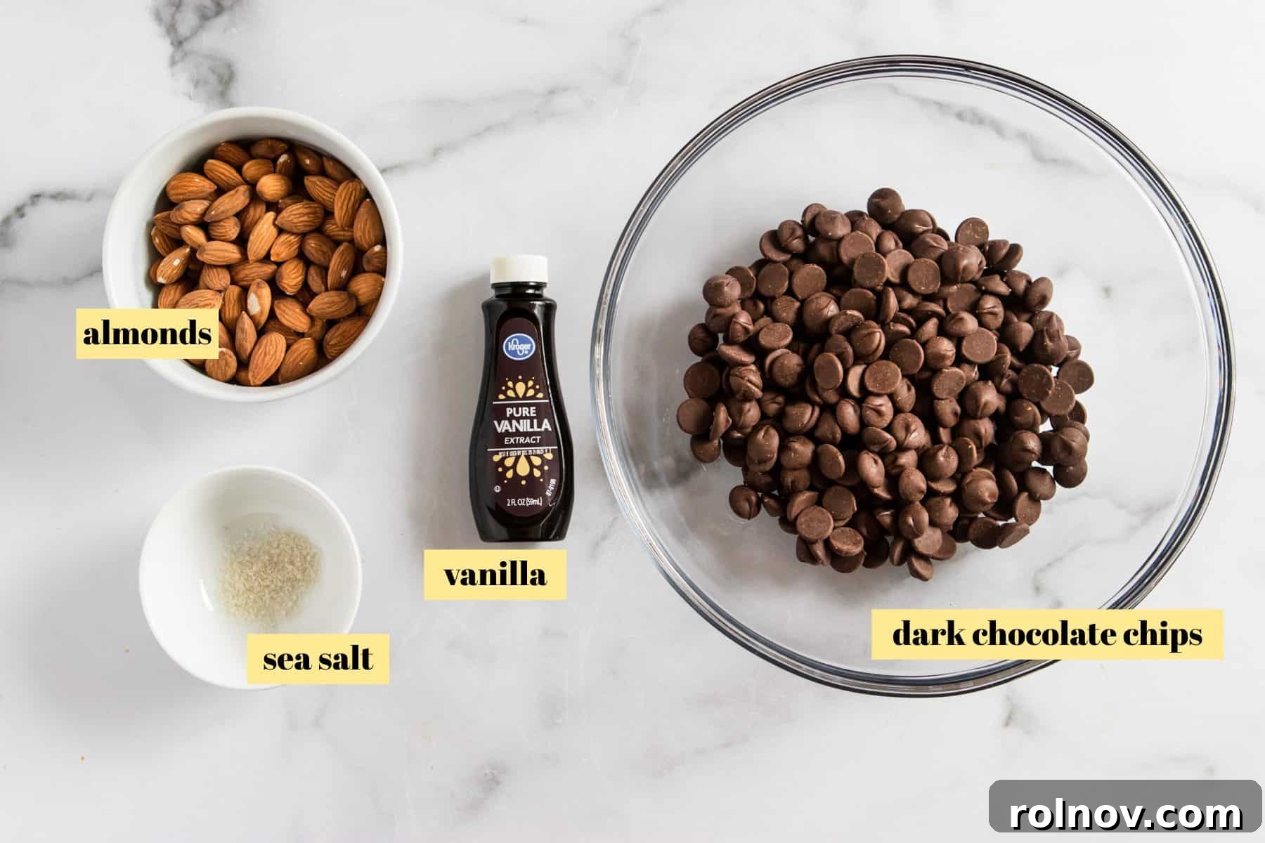Sweet and Salty Dark Chocolate Almond Bark Thins 4 Ingredients for making dark chocolate almond bark, including chocolate chips, almonds, vanilla, and sea salt, laid out on a clean surface.