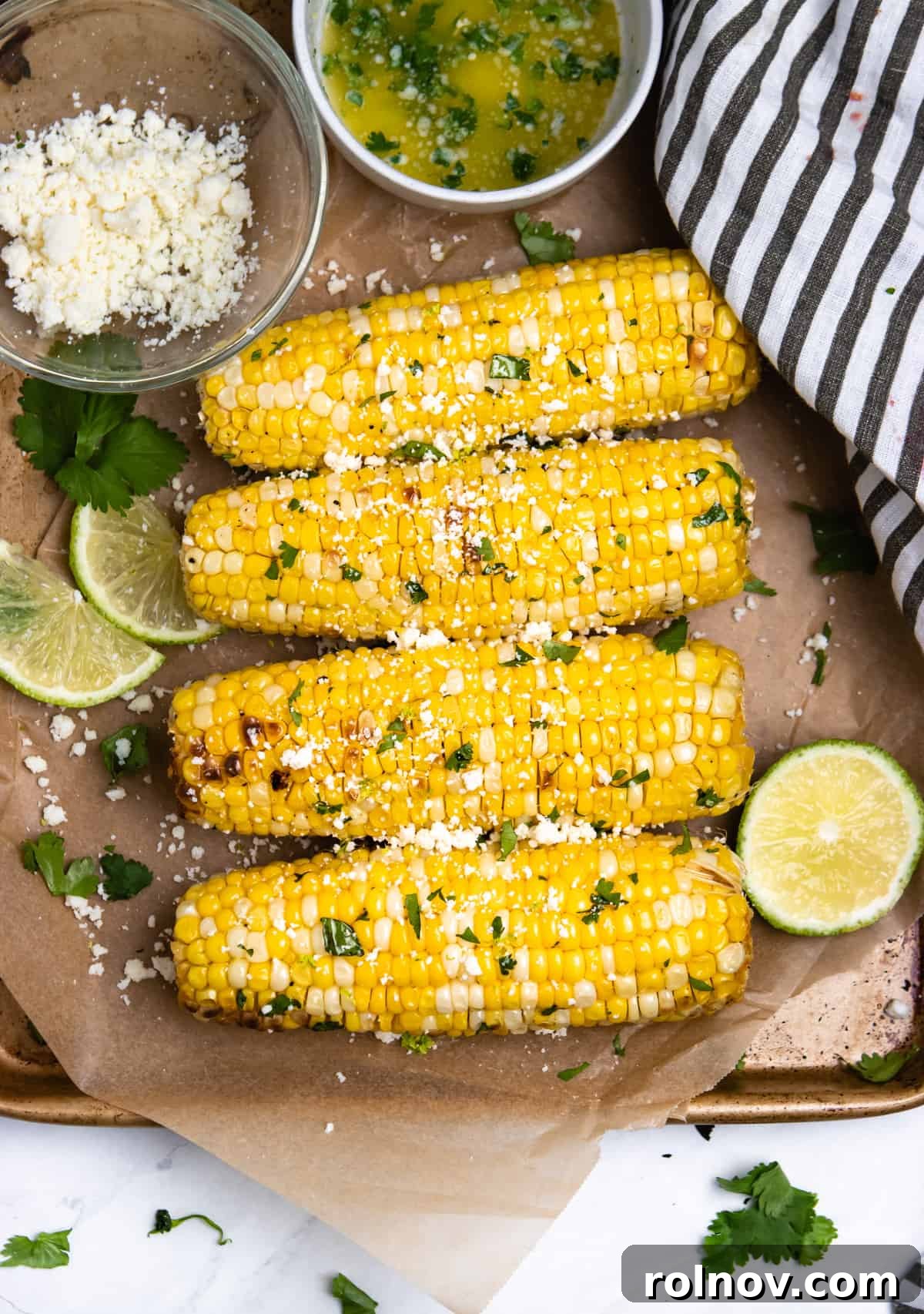 Air Fried Corn on the Cob with Zesty Cilantro Lime Butter Glaze 2 Overview of air-fried corn on the cob with limes and cotija cheese on parchment paper, ready to serve.