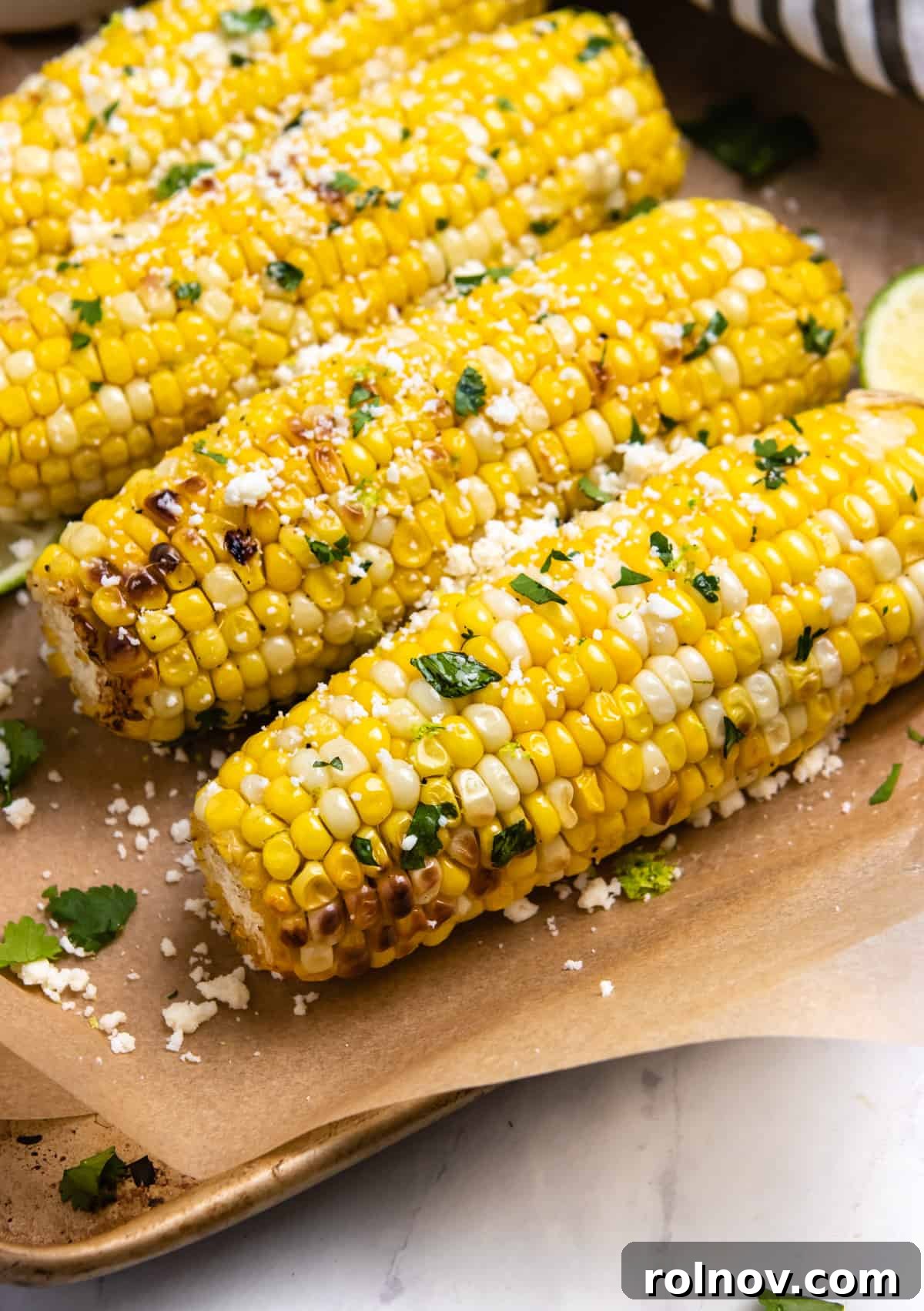 Air Fried Corn on the Cob with Zesty Cilantro Lime Butter Glaze 6 Beautifully air-fried corn on the cob, garnished with melting butter and fresh cilantro, presented on brown parchment paper.