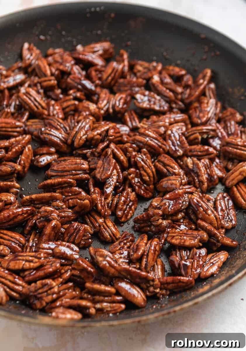 Cooked maple candied pecans in a nonstick skillet, showing the absorbed maple syrup and a shiny, caramelized coating, indicating they are almost ready.