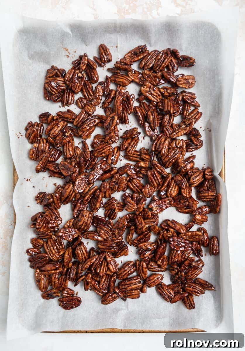 Maple candied pecans spread in a single, even layer on a parchment-lined cookie sheet for cooling and hardening.