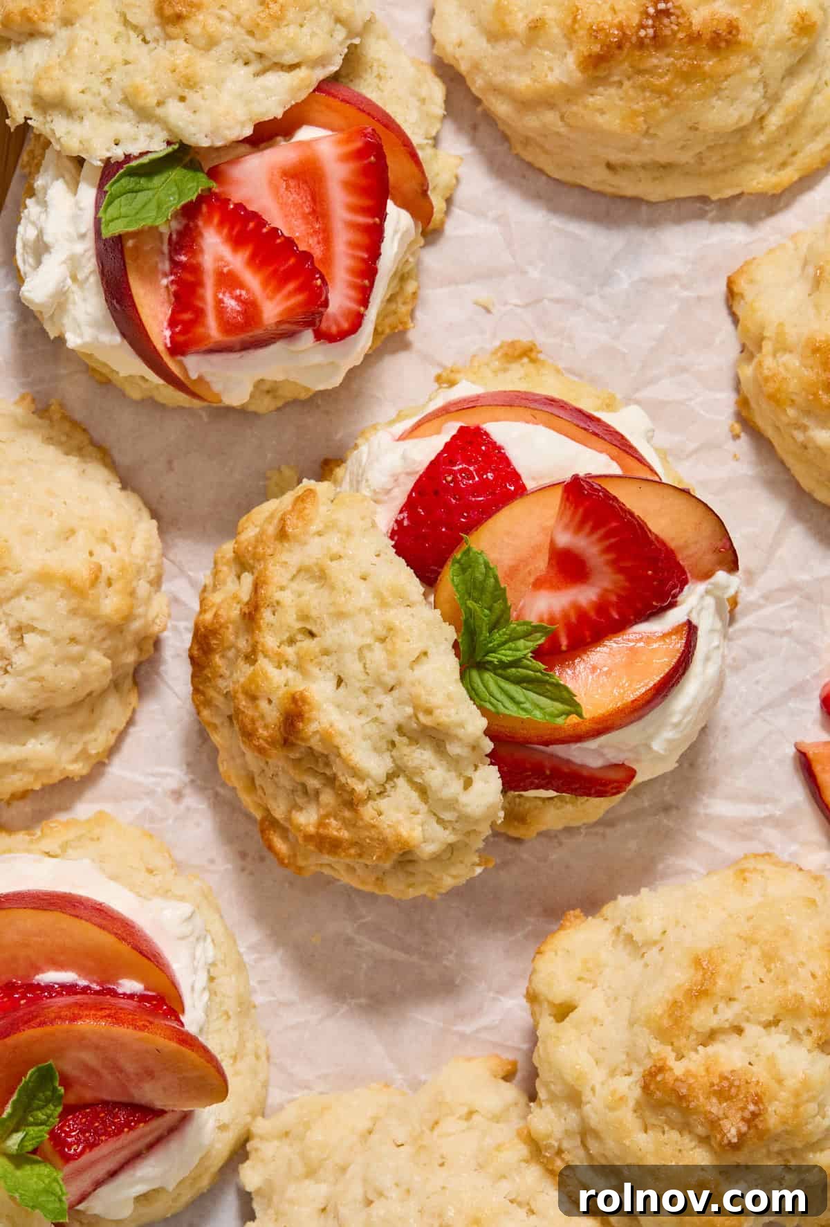 Sun-Kissed Peach Strawberry Shortcake 12 Overhead view of strawberry peach shortcakes with buttermilk biscuit tops propped to the side to show fruit and mint leaves on whipped cream.