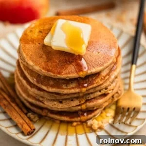 Spiced Apple Oat Pancakes 13 Stack of pancakes on plate with butter and maple syrup and cinnamon sticks beside.