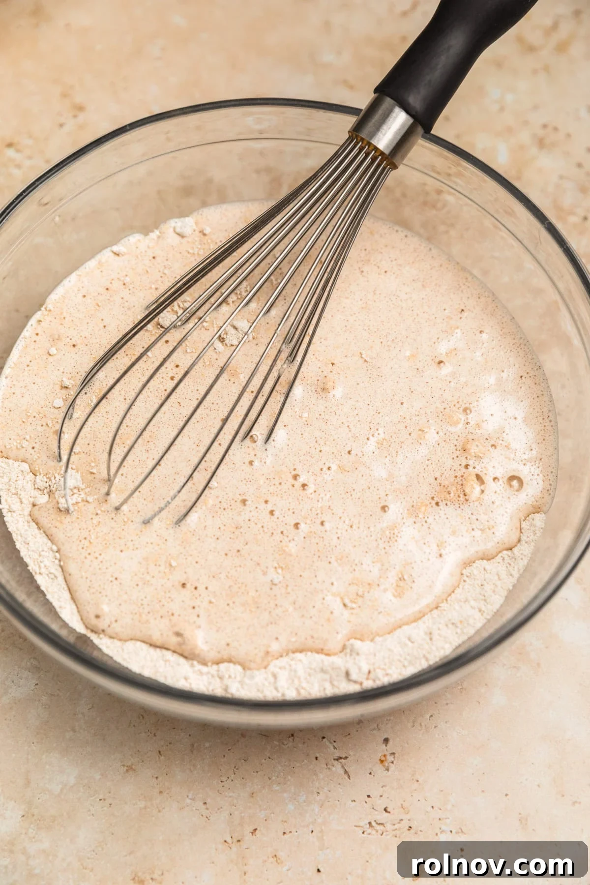 Spiced Apple Oat Pancakes 9 Wet and dry ingredients added to mixing bowl with whisk, showing a developing pancake batter.
