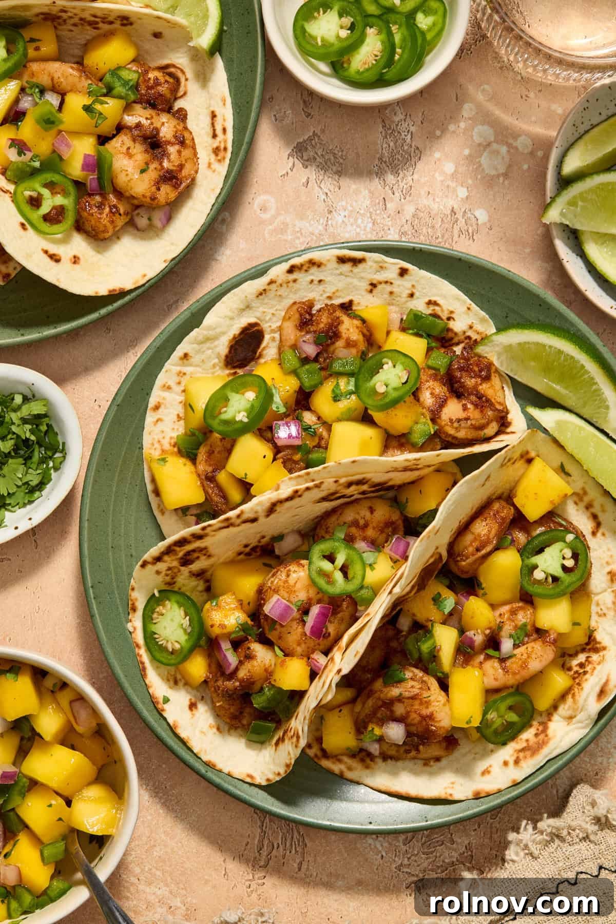Tropical Shrimp Tacos with Mango Salsa 2 Spicy shrimp tacos on a vibrant green plate, generously topped with fresh mango salsa, garnished with sliced jalapeños and accompanied by lime wedges.