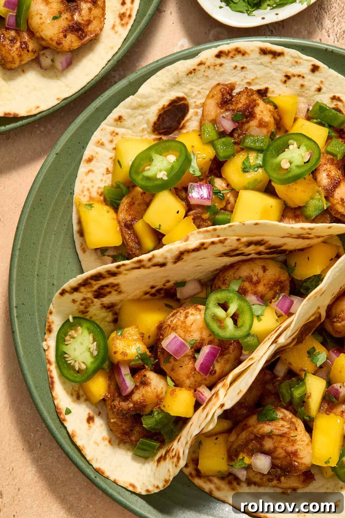 Tropical Shrimp Tacos with Mango Salsa 13 A tantalizing view of assembled shrimp tacos on a green plate, generously filled with spicy shrimp and topped with vibrant mango salsa, ready to be devoured.