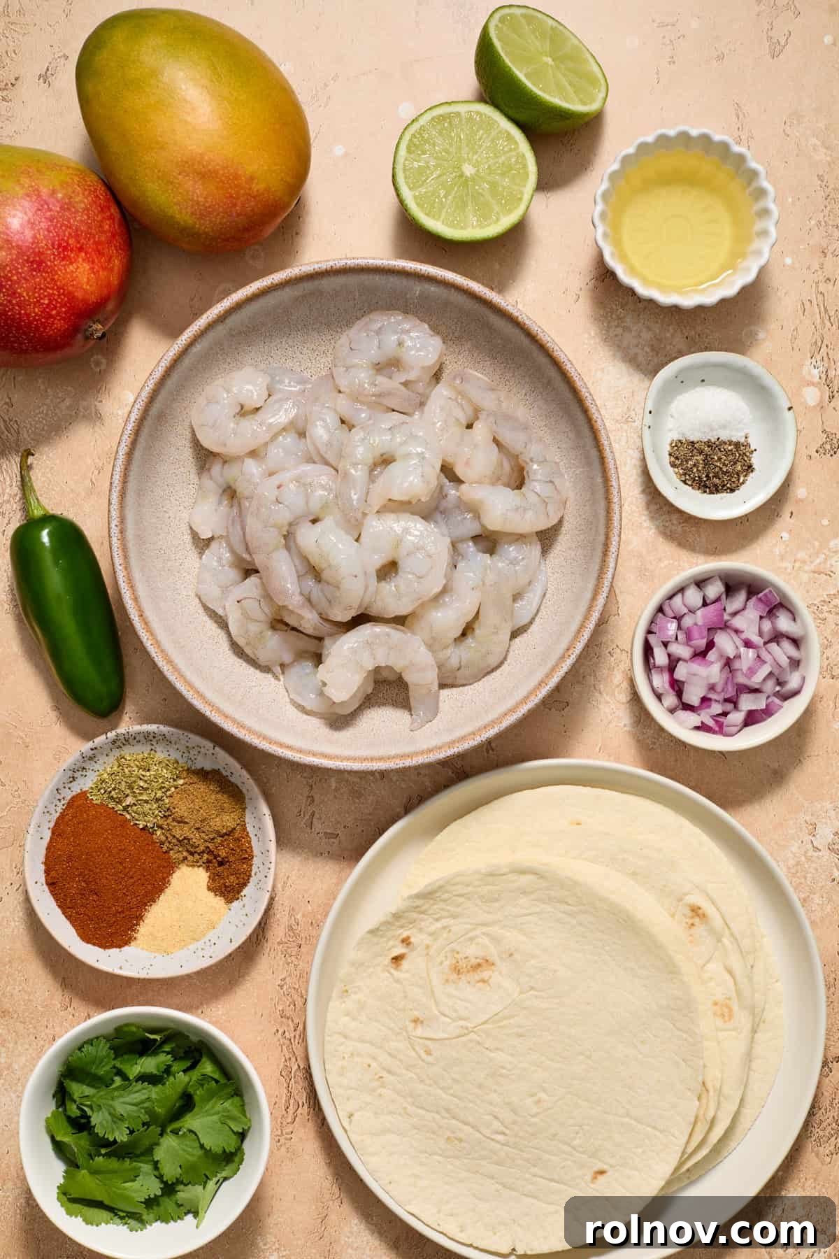 Tropical Shrimp Tacos with Mango Salsa 4 A colorful array of raw shrimp, ripe mangoes, various spices, fresh tortillas, and bright limes arranged beautifully on a surface, ready for cooking.
