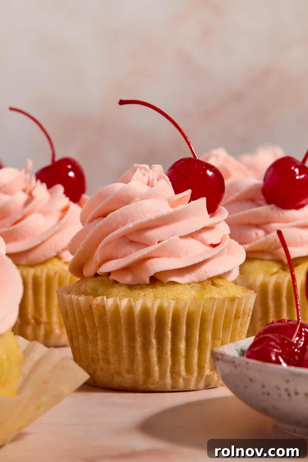 Golden Pineapple Cherry Bliss 2 Cherry frosted pineapple cupcakes arranged on surface with maraschino cherry on top.