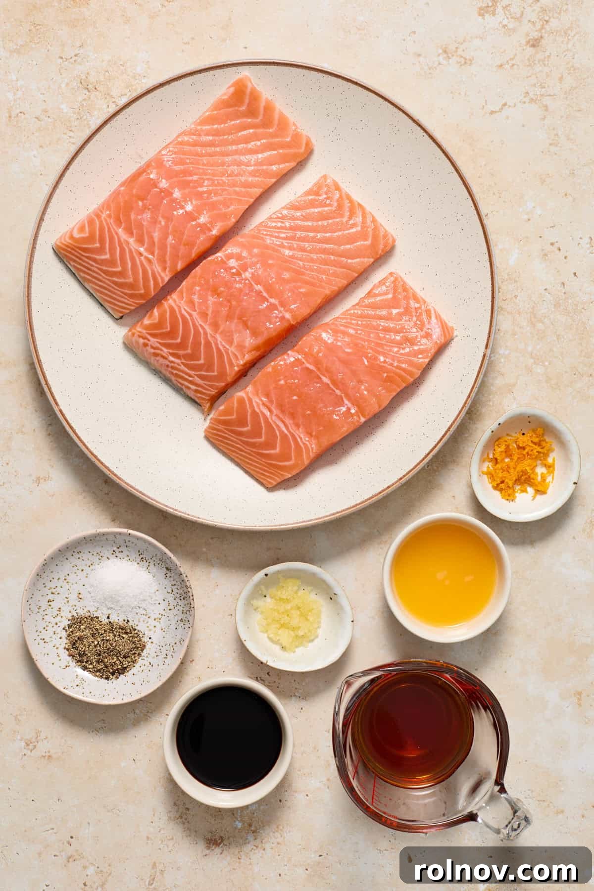Salmon, orange zest, maple syrup and other ingredients arranged on surface to make glazed salmon.