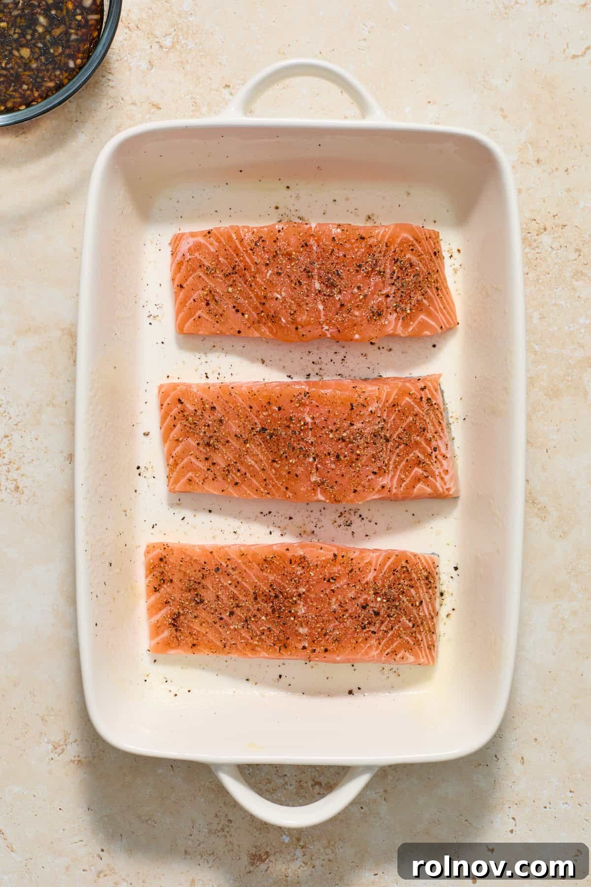 Salmon fillets in white baking pan seasoned with salt and pepper.