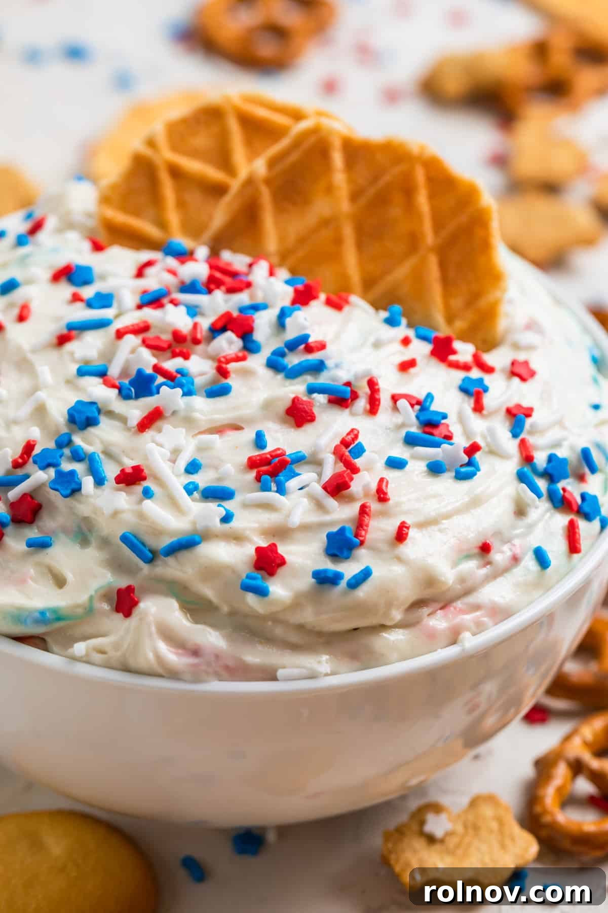 Celebration Funfetti Dip 2 White bowl with red, white and blue funfetti cake dip with waffle cookie pieces dipped in.