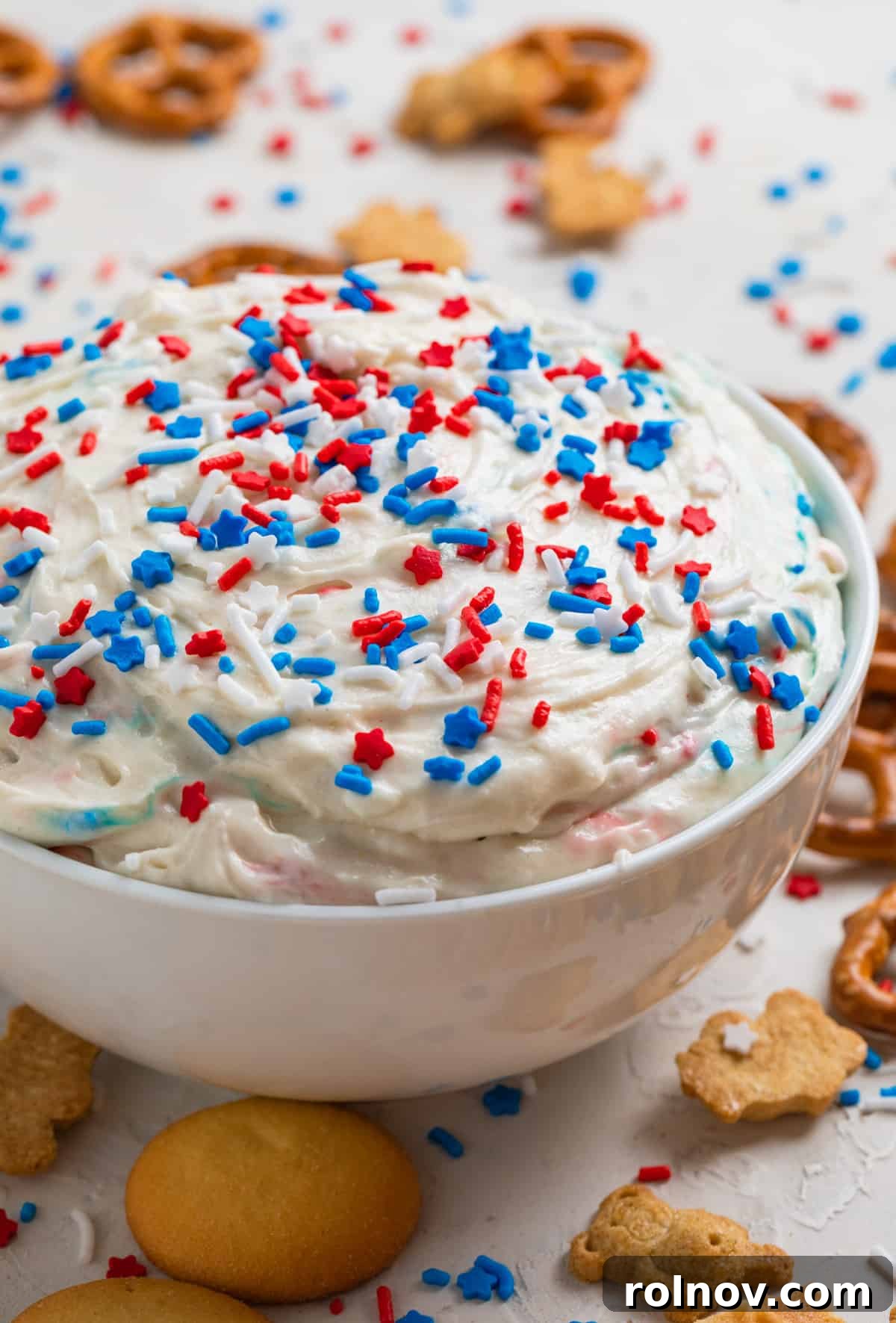 Celebration Funfetti Dip 9 Red, white and blue patriotic funfetti dip in white bowl with sprinkles on top and cookies surrounding.